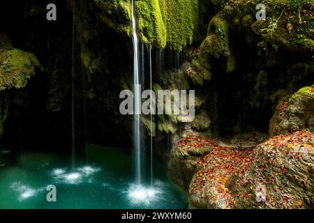 Eine ruhige Szene der Wasserfälle am Urederra River, umgeben von üppigen Buchenwäldern in Urbasa, Navarra, mit herbstlichen Blättern verstreut Stockfoto