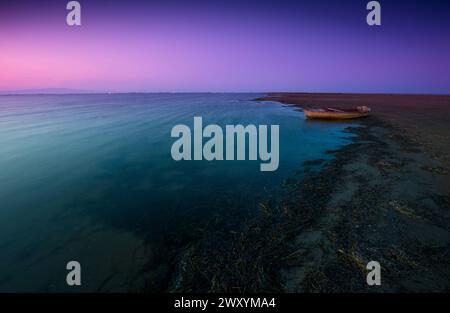 Über dem Delta del Ebro herrscht eine ruhige Abenddämmerung mit einem einsamen Boot, das bei Ebbe auf dem Gefälle von blauem bis violettem Wasser ruht Stockfoto