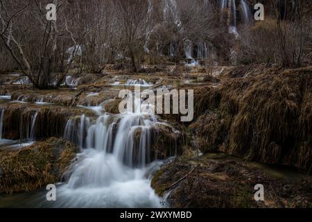 Eine friedliche Szene mit mehreren kaskadierenden Wasserfällen, die während der Wintersaison über moosige Felsen in einem ruhigen, blattlosen Wald fließen Stockfoto