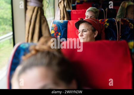 Eine reife Frau mit rotem Hut sitzt in einem Bus, blickt nachdenklich aus dem Fenster und verkörpert einen Moment der Reise-Reflexion Stockfoto