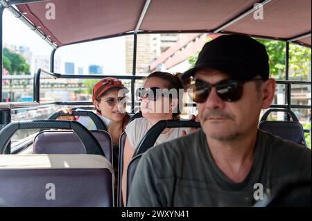 Drei Touristen werden bei einer Stadtbesichtigung in einem Bus mit offenem Oberdeck gefangen, wobei ihr Schwerpunkt auf ihren Ausdruck und ihre Umgebung liegt Stockfoto