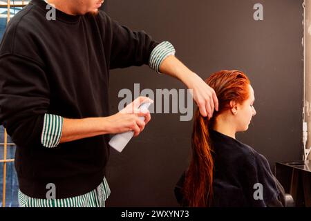 Professionelle Friseurin sprüht und kämmt das lange, dunkelbraune Haar einer Frau, um das Styling in einem modernen Friseursalon vorzubereiten Stockfoto