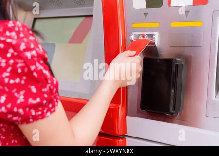 Nahaufnahme einer Frauenhand, die eine rote Debitkarte in einen Geldautomaten einsetzt Stockfoto