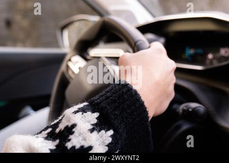 Nahaufnahme der Hand einer Person, die einen Winterhandschuh trägt, während sie ein Lenkrad hält und das Fahren eines Fahrzeugs bei kaltem Wetter zeigt Stockfoto