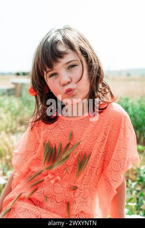 Ein Mädchen im Korallenkleid macht einen verspielten Stupf, während es Kiefernzweige hält und den fröhlichen Sommer auf dem Bauernhof verkörpert Stockfoto