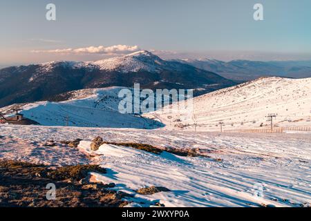 Glühender Sonnenuntergang über den schneebedeckten Gipfeln und Hängen der Sierra de Guadarrama in der Nähe von Madrid, mit Spuren von Winteraktivitäten Stockfoto