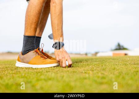 Seitenansicht der beschnittenen, nicht erkennbaren Nahaufnahme der Beine eines Golfspielers, während er den Golfball auf einem gut gepflegten Rasen platziert, bereit für einen Schaukel. Stockfoto