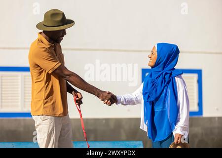 Ein vielseitiges Paar begrüßt sich mit einem Handschlag unter hellem Sonnenlicht und symbolisiert Freundschaft und kulturelle Vielfalt Stockfoto