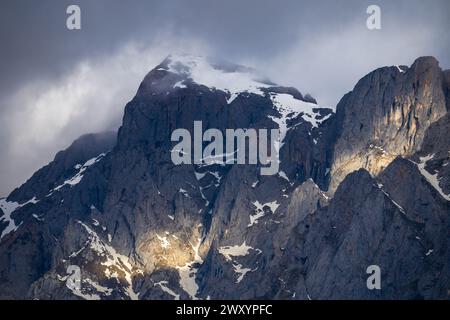 Sonnendurchflutete Gipfel ragen über das zerklüftete Gelände des Nationalparks Picos de Europa, bedeckt von Schnee und Wolken. Stockfoto