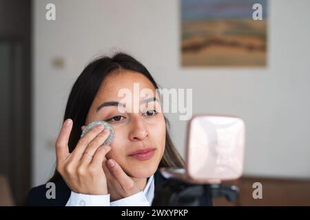Eine junge Frau nimmt ein wiederverwendbares Make-up-Entferner-Pad auf ihrem Gesicht auf und nimmt ein Tutorial auf Stockfoto