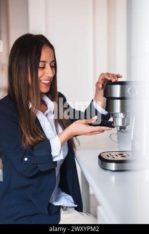 Eine fröhliche Frau wird beobachtet, wie sie Kaffee mit einer modernen Espressomaschine in einer hellen Küche zubereitet Stockfoto