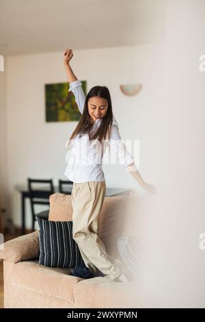 Eine fröhliche junge Frau tanzt gern allein in einem hellen Wohnzimmer und drückt Glück und Freiheit aus Stockfoto