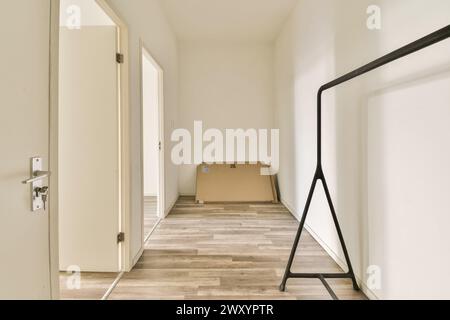 Ein leerer, heller Raum mit offener Tür, hellen Wänden und Holzlaminatböden mit minimalistischem Metallgarderobe. Stockfoto