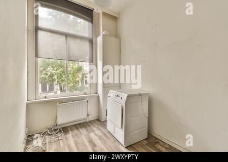 Ein unmöbliertes Zimmer mit einer Waschmaschine, großem Fenster und Gebrauchsspuren an den Wänden. Stockfoto