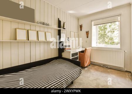 Ein gut beleuchtetes Schlafzimmer mit moderner Einrichtung für das Home Office, mit Schreibtisch, Stuhl und Regalen, minimalistischer Einrichtung und großem Fenster. Stockfoto