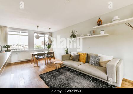 Helles, modernes Wohnzimmer mit komfortablem Sofa, Esstisch, Holzfußboden und großen Fenstern für viel Tageslicht. Stockfoto