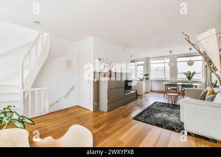 Geräumiges, modernes Wohnzimmer mit Holzboden, Wendeltreppe, viel Tageslicht und stilvollen Möbeln. Stockfoto