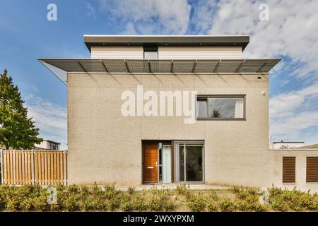 Ein modernes zweistöckiges Wohnhaus mit flachem Dach, großen Fenstern und einer Backsteinfassade, vor einem klaren Himmel gelegen, mit einem kleinen Garten im for Stockfoto