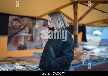 Junge Blondine wegen der Winterkälte auf der Stadtmesse mit handwerklichem Lebensmittelmarkt. Stockfoto
