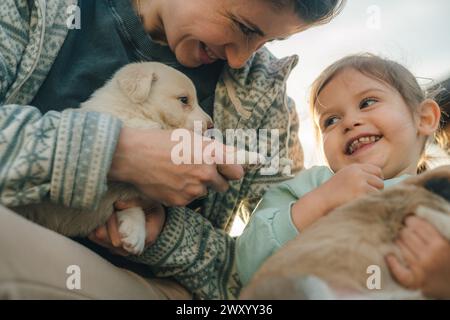 Niedliches, kleines Mädchen und ihre Mutter halten zwei Welpen. Kinder- und Haustierkonzept Stockfoto