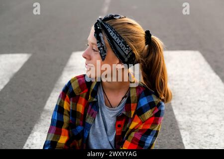 Porträt eines Teenagers, das ein stilvolles Bandana und ein fröhliches Lächeln trägt, selbstbewusst auf einer Landstraße steht und Jugendlichkeit und ein Gefühl für ausstrahlt Stockfoto