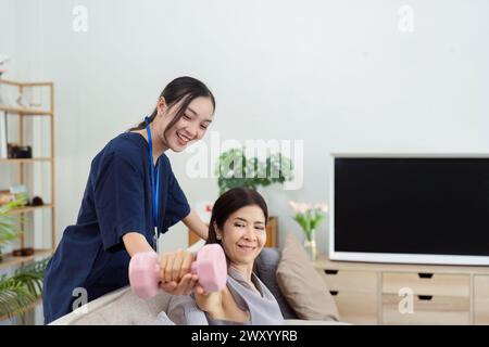 Asiatische ältere Frau, die Physiotherapeutin mit Unterstützung von Krankenschwester oder Pflegekraft macht. Ältere Frau mit Kurzhanteln-Trainingsübungen für Patienten mit Stockfoto