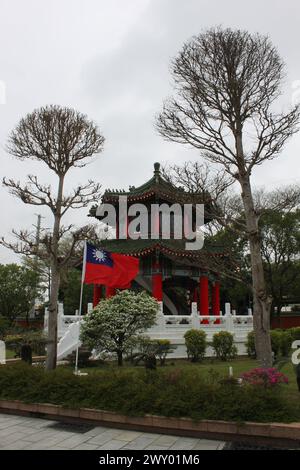 Taipeh, Taiwan, 26. März 2024: Taiwanesische Flagge am Nationalen Revolutionären Märtyrerschrein zwischen Bäumen im frühen Frühjahr, düsterer Tag. Stockfoto