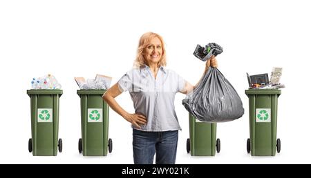 Lächelnde reife Frau, die einen Plastikmüllbeutel vor Recyclingbehältern hält, isoliert auf weißem Hintergrund Stockfoto