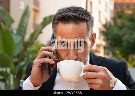 Porträt eines lächelnden Geschäftsmannes, der draußen mit einem Smartphone spricht. Stockfoto
