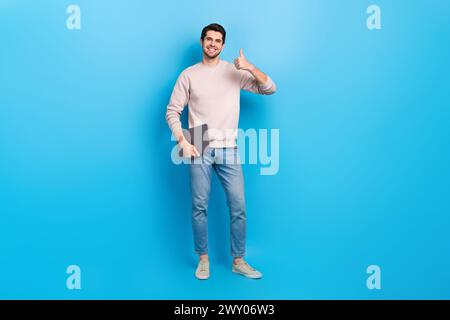 Foto von einem angenehmen gutaussehenden, fröhlichen Kerl gekleideten weißen Pullover, der Laptop hält, der Daumen nach oben zeigt, schöne Arbeit isoliert auf blauem Hintergrund Stockfoto