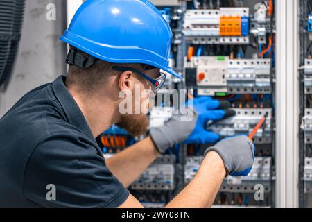 Ein Elektriker arbeitet in einer Schalttafel mit einem elektrischen Anschlusskabel. Stockfoto