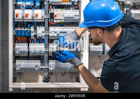 Ein Elektriker arbeitet in einer Schalttafel mit einem elektrischen Anschlusskabel. Stockfoto