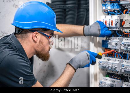 Ein Elektriker arbeitet in einer Schalttafel mit einem elektrischen Anschlusskabel. Stockfoto