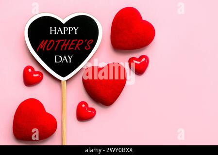 Alles Gute zum Muttertag. Holzherz mit dem Text Happy Mother's Day mit roten Herzen auf rosa Hintergrund Stockfoto