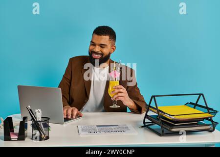 Ein Mann sitzt an einem Schreibtisch mit offenem Laptop, begleitet von einem Drink. Er scheint konzentriert und engagiert in seiner Arbeit zu sein. Stockfoto