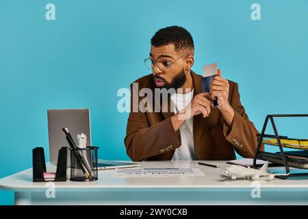 Ein fokussierter Mann, der tief in Gedanken an einem Schreibtisch sitzt, eine Kreditkarte in der Hand hält und über einen Kauf oder eine finanzielle Entscheidung nachdenkt. Stockfoto