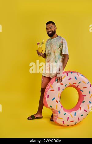 Ein Mann steht in Ehrfurcht neben einem riesigen Donut, der von seiner Größe klein ist. Der Donut ist bunt und verlockend und bettelt darum, gegessen zu werden. Stockfoto