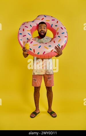 Ein Mann mit einem riesigen Donut in der einen Hand und einem Glas Bier in der anderen, der die köstliche Kombination aus süßen und herzhaften Aromen genießt. Stockfoto