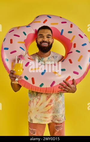 Ein Mann hält freudig einen riesigen Donut in der einen Hand und ein Glas Bier in der anderen und genießt den leckeren und genussvollen Moment. Stockfoto