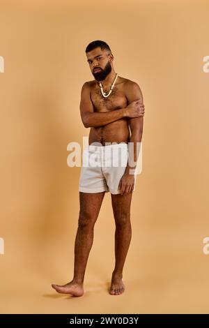 Ein Mann in weißen Shorts steht mit einer selbstbewussten Haltung und kreuzt die Arme mit einem ruhigen Gesichtsausdruck. Stockfoto