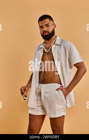 Ein Mann in weißen Shorts und einem Hemd geht anmutig am Sandstrand entlang, die ruhigen Wellen schlagen sanft am Ufer hinter ihm. Stockfoto