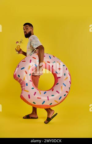 Ein Mann hält freudig einen gigantischen Donut in der einen Hand und ein Glas Bier in der anderen und präsentiert eine einzigartige und köstliche Kombination von Leckereien. Stockfoto