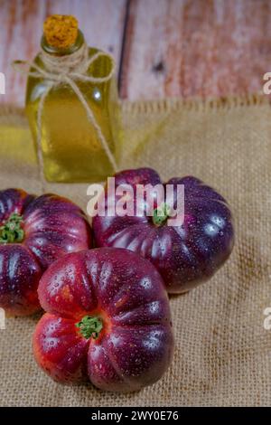 Gruppe von leckeren frischen Tomaten der blauen Sorte auf einem Sacklappen mit einer Flasche Olivenöl im Hintergrund Stockfoto