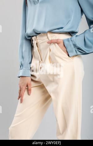 Modemodell in beiger Hose und blauer Bluse mit Hand in der Tasche auf isoliertem Hintergrund. Geeignet für Modenwerbung. Stockfoto