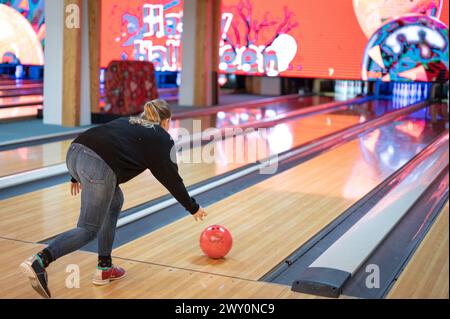 Sequenz, in der die Bowlingnadel auf die Bahn geschleudert wird. Wurftechnik eines jungen Mädchens. Sie übt mit dem rosa Ball, der leicht ist. Stockfoto