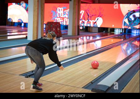 Sequenz, in der die Bowlingnadel auf die Bahn geschleudert wird. Wurftechnik einer langhaarigen blonden jungen Frau in schwarz gekleidet. Stockfoto