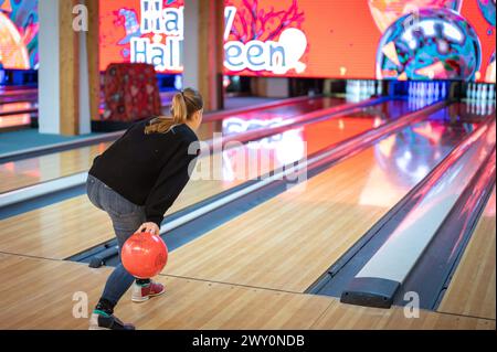 Sequenz, in der die Bowlingnadel auf die Bahn geschleudert wird. Wurftechnik einer langhaarigen blonden jungen Frau in schwarz gekleidet. Stockfoto