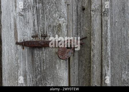 Nahaufnahme des alten rostigen Vorhängeschlosses auf einer alten grauen Holztür. Stockfoto