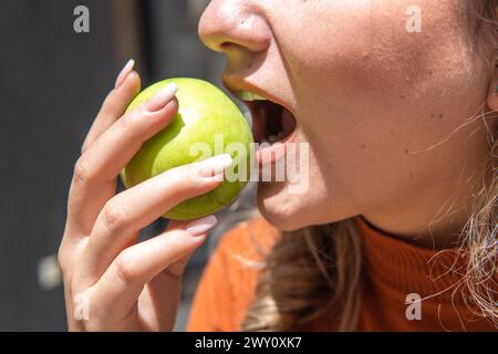 Nahaufnahme des Mundes einer nicht erkennbaren Frau, die morgens mit der Hand einen grünen Apfel isst Stockfoto