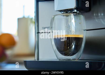 Frischer Espresso in klarem Glas am Morgen. Kaffeemaschine in der Küche, Nahaufnahme. Moderne Kaffeemaschine mit frisch gebrühtem Kaffee in Glasbecher. Küche ap Stockfoto